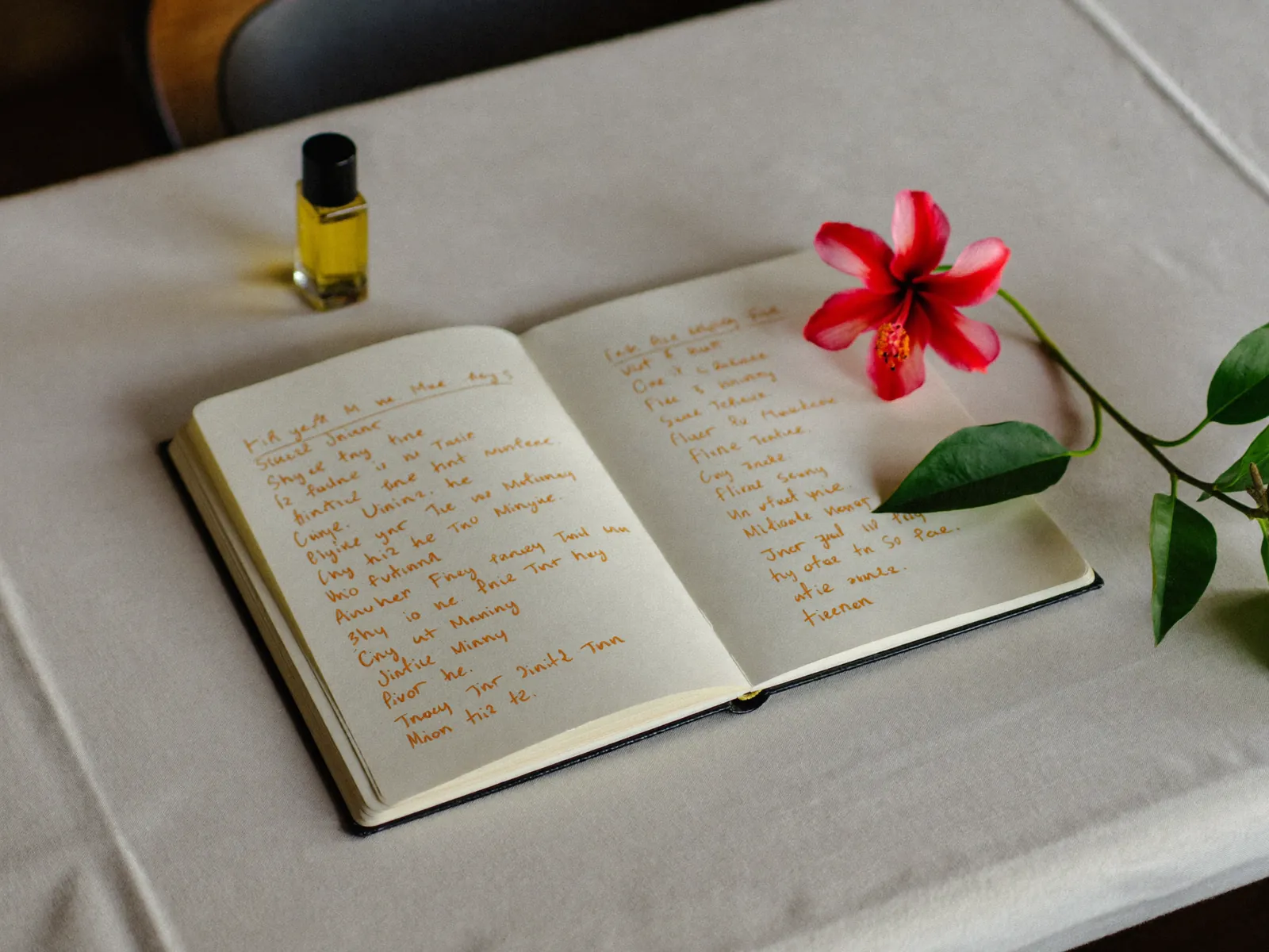 An open notebook of handwritten scent notes with a hibiscus flower and a vial of oil